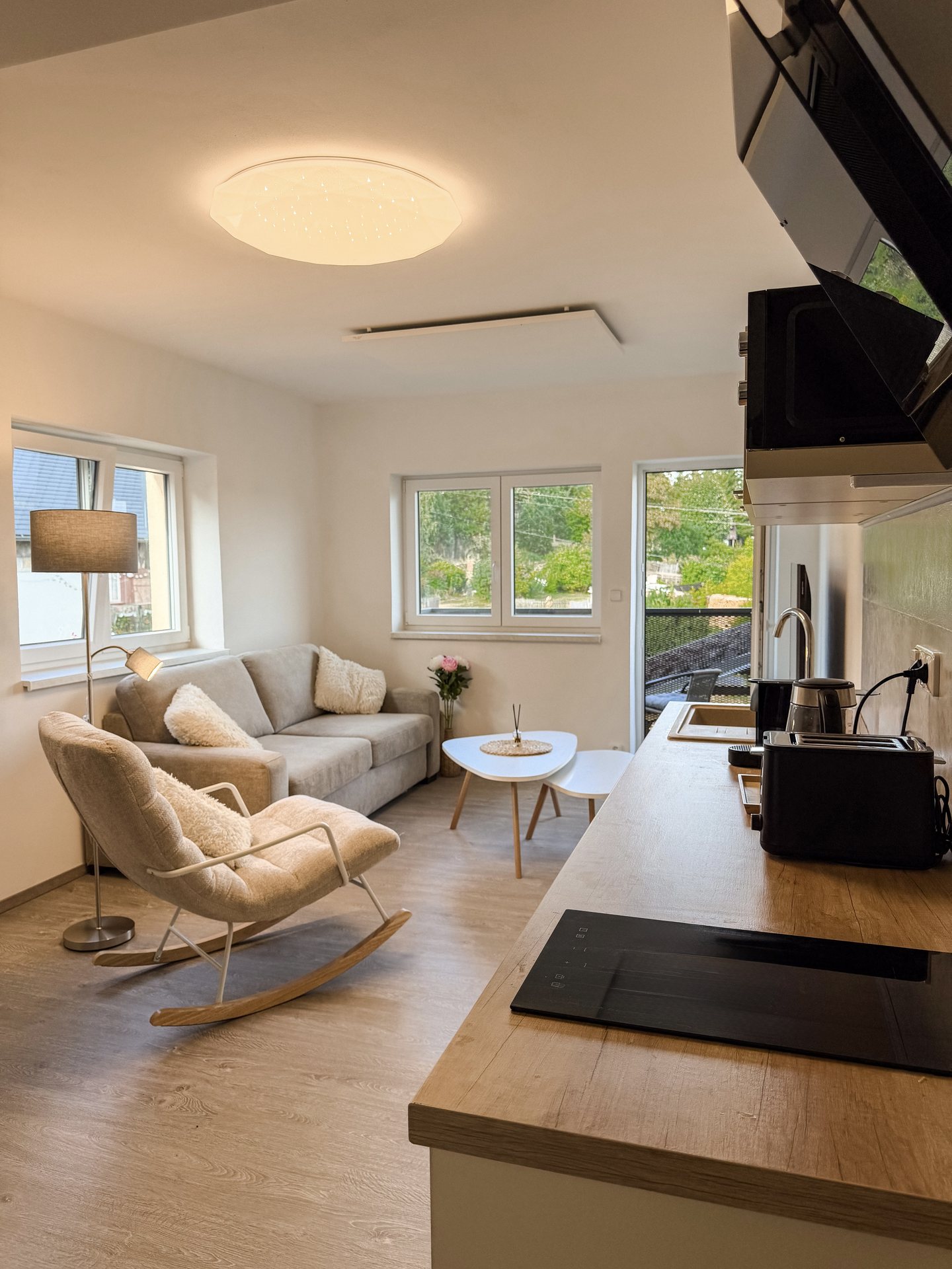 Moderní obývací pokoj s houpacím křeslem, pohovkou a vstupem na balkon – Apartmány Panorama